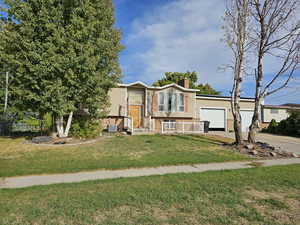 Bi-level home featuring concrete driveway, brick siding, a chimney, a front yard, and an attached garage
