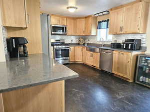 Kitchen featuring tasteful backsplash, light brown cabinetry, appliances with stainless steel finishes, dark marble finish flooring, and a textured ceiling