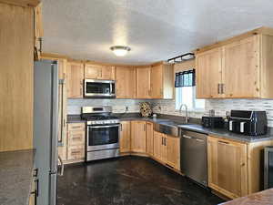 Kitchen featuring appliances with stainless steel finishes, decorative backsplash, light brown cabinets, and a textured ceiling