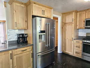 Kitchen with decorative backsplash, light brown cabinets, a textured ceiling, stainless steel appliances, and dark stone countertops