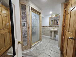 Full bath with a textured ceiling, light tile patterned floors, a stall shower, tile walls, and wainscoting
