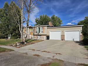 View of front of property featuring brick siding, a chimney, concrete driveway, and an attached garage
