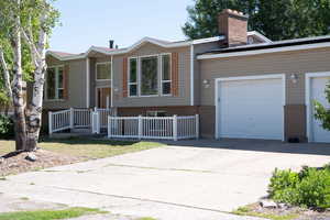 Raised ranch with brick siding, driveway, a chimney, and an attached garage