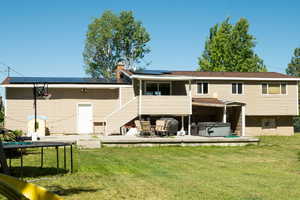 Back of house with a hot tub, solar panels, a yard, a deck, and a chimney