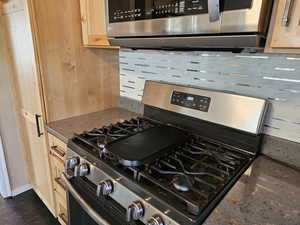 Kitchen featuring light brown cabinets, appliances with stainless steel finishes, tasteful backsplash, and dark stone counters
