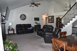 Carpeted living area featuring high vaulted ceiling, stairs, and ceiling fan