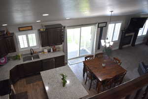 Kitchen featuring dark brown cabinets, a textured ceiling, granite counters, stainless steel dishwasher, and pendant lighting