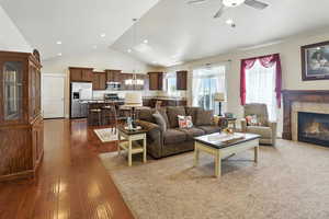 Living area with a chandelier, high vaulted ceiling, dark wood finished floors, a tiled fireplace, and a ceiling fan