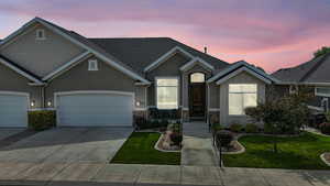 View of front facade featuring driveway, a yard, stone siding, roof with shingles, and an attached garage