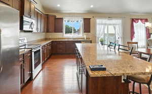Kitchen with a breakfast bar area, stainless steel appliances, light stone counters, a kitchen island, and recessed lighting