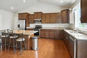 Kitchen featuring stainless steel appliances, light stone countertops, a breakfast bar, dark wood-style floors, and vaulted ceiling