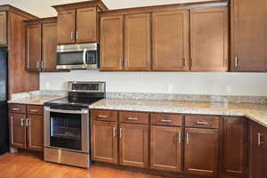 Kitchen featuring appliances with stainless steel finishes, light stone countertops, light wood-style floors, and brown cabinets