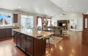 Kitchen featuring a kitchen breakfast bar, light stone counters, pendant lighting, a center island, and dark wood-style flooring