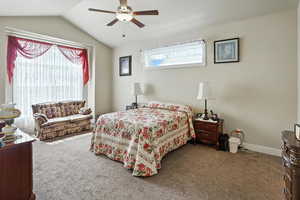 Carpeted bedroom with a ceiling fan and vaulted ceiling