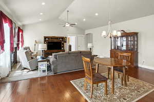 Dining area featuring healthy amount of natural light, dark wood-type flooring, a chandelier, ceiling fan, and high vaulted ceiling