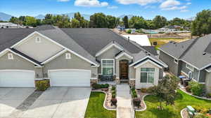 View of front facade with roof with shingles, stone siding, driveway, a front yard, and stucco siding