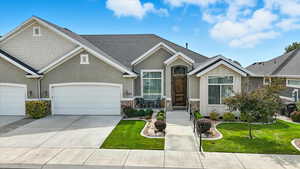 View of front facade featuring a front lawn, roof with shingles, concrete driveway, stone siding, and an attached garage
