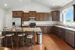 Kitchen featuring stainless steel appliances, a kitchen bar, dark wood-type flooring, a kitchen island, and light stone counters