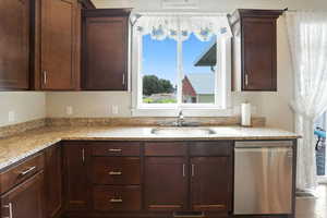 Kitchen with stainless steel dishwasher, light stone countertops, and dark brown cabinets