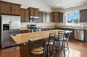Kitchen featuring dark brown cabinets, stainless steel appliances, a kitchen island, a breakfast bar area, and light stone countertops