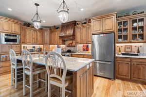 Kitchen with appliances with stainless steel finishes, a kitchen breakfast bar, light stone counters, a kitchen island with sink, and light wood finished floors