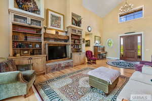 Living area with light wood finished floors, high vaulted ceiling, a stone fireplace, and a chandelier