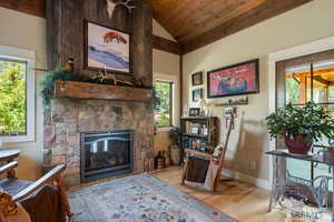 Living area featuring wood finished floors, lofted ceiling, wooden ceiling, and a stone fireplace