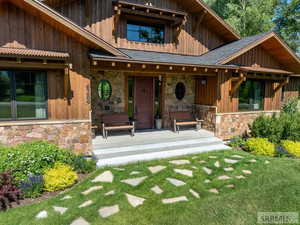Property entrance featuring stone siding, covered porch, and board and batten siding