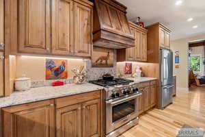 Kitchen with premium appliances, tasteful backsplash, premium range hood, light wood-style flooring, and light stone counters