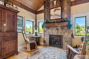 Sitting room featuring vaulted ceiling, light wood-type flooring, a stone fireplace, and wooden ceiling