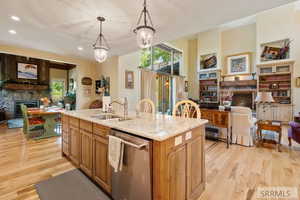 Kitchen with open floor plan, a fireplace, light stone counters, stainless steel dishwasher, and an island with sink