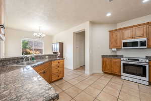 Kitchen with a textured ceiling, white appliances, brown cabinetry, light tile patterned floors, and a chandelier
