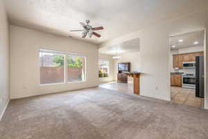 Unfurnished living room featuring light colored carpet, a ceiling fan, a chandelier, and a textured ceiling