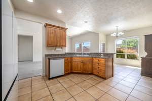 Kitchen featuring brown cabinets, stainless steel dishwasher, a textured ceiling, freestanding refrigerator, and healthy amount of natural light