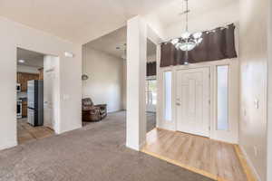 Entryway with a chandelier, light carpet, and light wood-type flooring