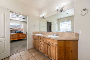 Ensuite bathroom featuring double vanity, light tile patterned floors, and ceiling fan