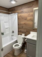 Full bathroom with shower / washtub combination, vanity, dark wood-style flooring, and wood walls