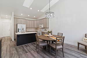 Dining space with a skylight, lofted ceiling, a chandelier, dark wood-type flooring, and recessed lighting