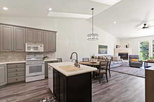 Kitchen with white appliances, lofted ceiling, recessed lighting, a premium fireplace, and hanging light fixtures