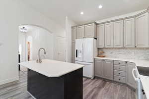 Kitchen with gray cabinetry, a center island with sink, white appliances, tasteful backsplash, and recessed lighting