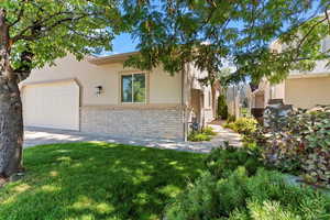 View of front facade with a garage, stucco siding, stone siding, a front yard, and driveway