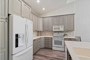 Kitchen with white appliances, gray cabinets, lofted ceiling, dark wood finished floors, and light stone countertops