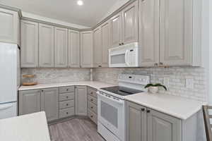 Kitchen with gray cabinets, white appliances, backsplash, light wood-style flooring, and recessed lighting