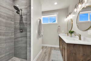 Full bathroom featuring double vanity, a tile shower, and light wood finished floors