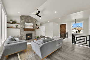 Living room featuring lofted ceiling, a fireplace, wood finished floors, a chandelier, and recessed lighting