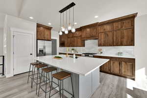 Kitchen with tasteful backsplash, an island with sink, a breakfast bar area, decorative light fixtures, and light wood finished floors