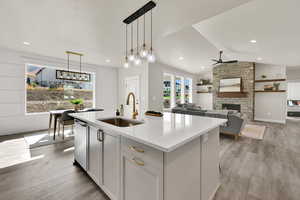 Kitchen with a stone fireplace, hanging light fixtures, light wood-style floors, lofted ceiling, and light stone countertops
