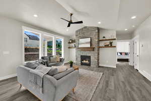 Living area with vaulted ceiling, a stone fireplace, wood finished floors, a ceiling fan, and recessed lighting