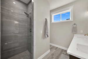 Bathroom featuring double vanity, tiled shower, and light wood-style floors