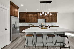 Kitchen with an island with sink, a breakfast bar, decorative light fixtures, tasteful backsplash, and recessed lighting